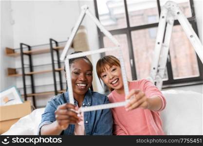 moving, people and real estate concept - happy smiling women with ruler folded in shape of house at new home. happy smiling women with ruler in shape of house