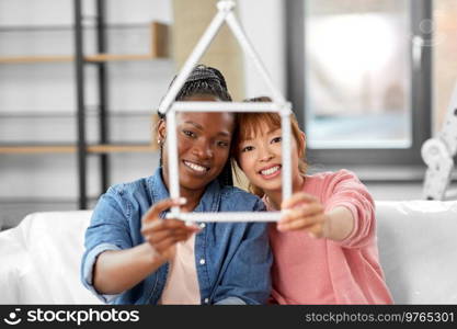 moving, people and real estate concept - happy smiling women with ruler folded in shape of house at new home. happy smiling women with ruler in shape of house