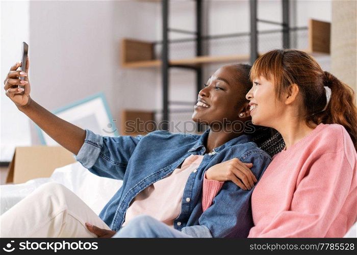 moving, people and real estate concept - happy smiling women with smartphone taking selfie at new home. women with smartphone taking selfie at new home