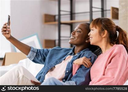 moving, people and real estate concept - happy smiling women with smartphone taking selfie at new home. women with smartphone taking selfie at new home