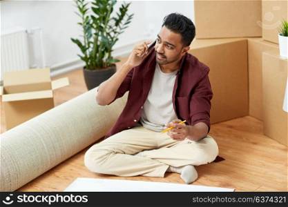 moving, people and real estate concept - indian man with blueprint and boxes at new home. man with blueprint and boxes moving to new home