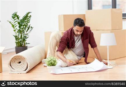 moving, people and real estate concept - indian man with blueprint and boxes at new home. man with blueprint and boxes moving to new home