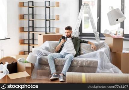 moving, people and real estate concept - man with smartphone and boxes at new home. man with smartphone and boxes moving into new home