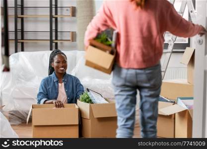 moving, people and real estate concept - woman unpacking boxes and her friend entering room at new home. woman unpacking boxes and moving to new home