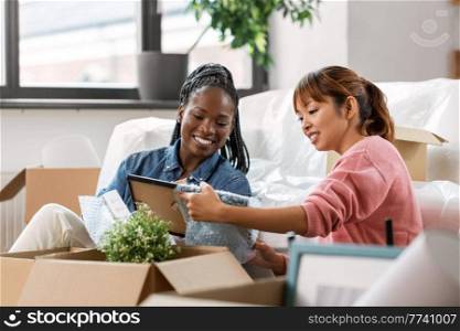 moving, people and real estate concept - women unpacking boxes at new home. women unpacking boxes and moving to new home