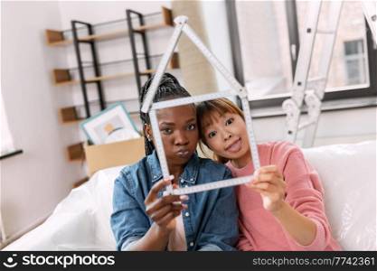 moving, people and real estate concept - women with ruler folded in shape of house making faces at new home. women with ruler in shape of house making faces