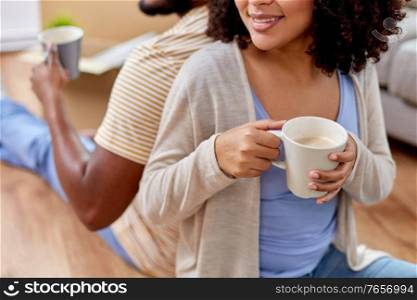 moving, people, repair and real estate concept - close up of happy african american couple sitting on sofa and drinking coffee at new home. happy couple drinking coffee moving to new home