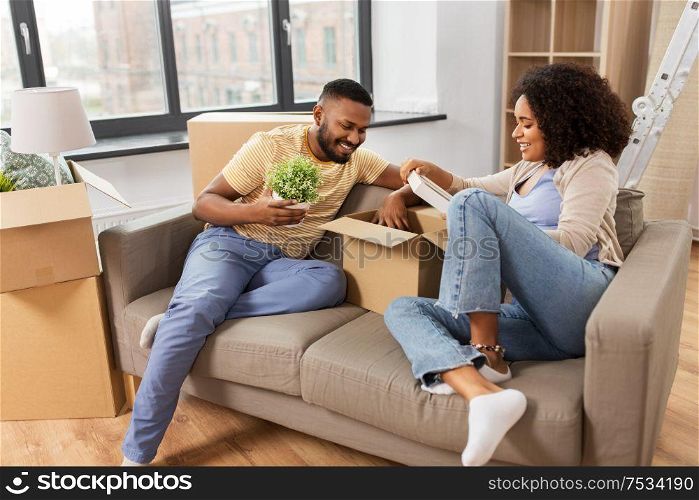 moving, people, repair and real estate concept - happy african american couple with photo frame and cardboard boxes sitting on sofa at new home. happy couple with boxes moving to new home
