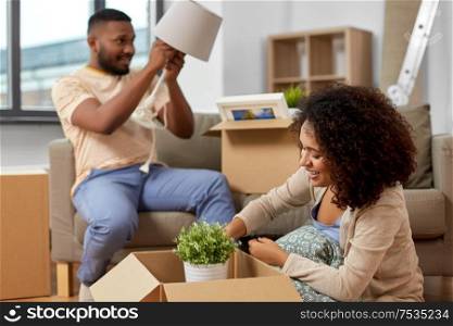moving, people, repair and real estate concept - happy african american couple with photo frame and cardboard boxes sitting on sofa at new home. happy couple packing boxes and moving to new home