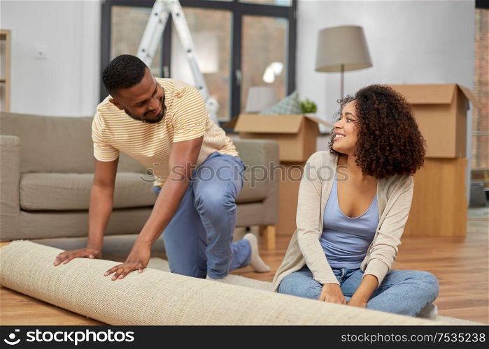 moving, people, repair and real estate concept - happy african american couple with carpet at new home. happy couple with carpet moving to new home