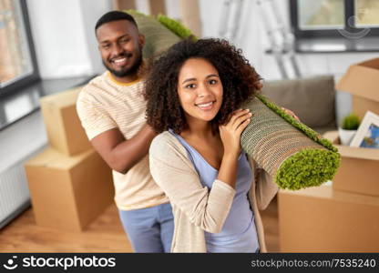 moving, people, repair and real estate concept - happy african american couple with carpet at new home. happy couple with carpet moving to new home