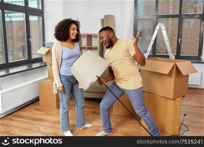 moving, people, repair and real estate concept - happy african american couple with lamp packing stuff into cardboard boxes at home and having fun. happy couple packing boxes and moving to new home