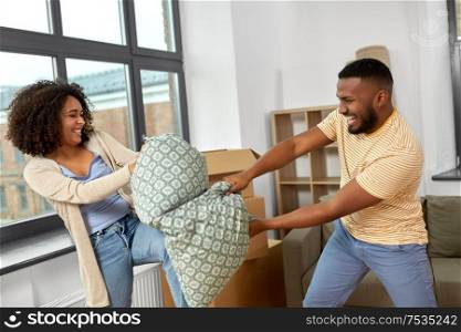moving, people, repair and real estate concept - happy african american couple having pillow fight at new home. happy couple having pillow fight at new home