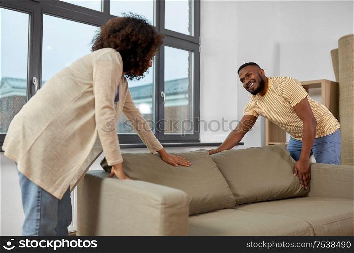 moving, people, repair and real estate concept - happy african american couple with sofa at new home. happy couple moving to new home