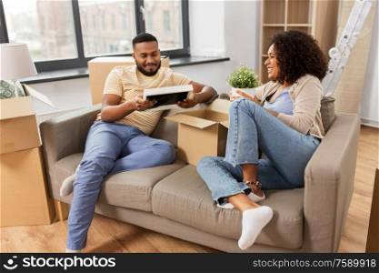 moving, people, repair and real estate concept - happy african american couple with photo frame and cardboard boxes sitting on sofa at new home. happy couple with boxes moving to new home