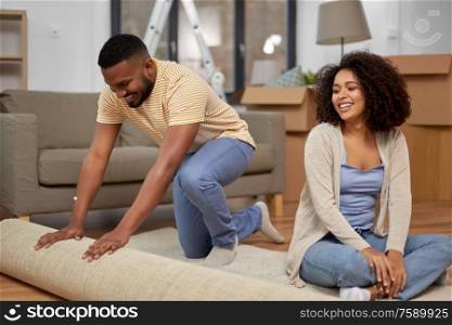 moving, people, repair and real estate concept - happy african american couple with carpet at new home. happy couple with carpet moving to new home