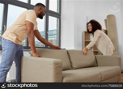 moving, people, repair and real estate concept - happy african american couple with sofa at new home. happy couple moving to new home