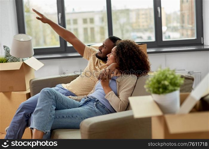 moving, people, repair and real estate concept - happy african american couple with cardboard boxes sitting on sofa at new home. happy couple with boxes moving to new home
