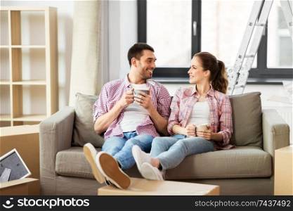 moving, people, repair and real estate concept - happy couple sitting on sofa and drinking coffee at new home. happy couple drinking coffee moving to new home
