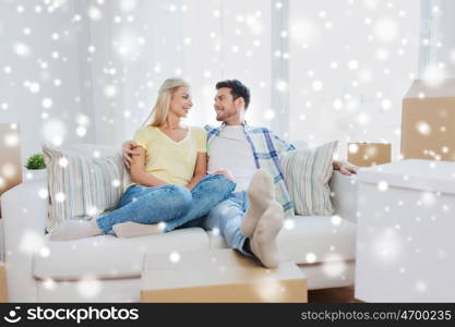 moving, people, repair and real estate concept - happy couple with cardboard boxes sitting on sofa at new home over snow