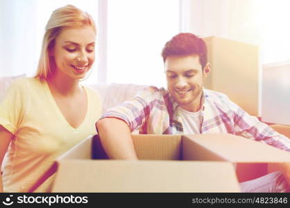 moving, people, repair and real estate concept - smiling couple looking into big cardboard box at new home