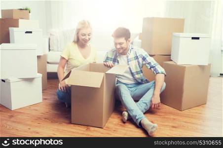 moving, people, repair and real estate concept - smiling couple looking into big cardboard box at new home. smiling couple with big boxes moving to new home