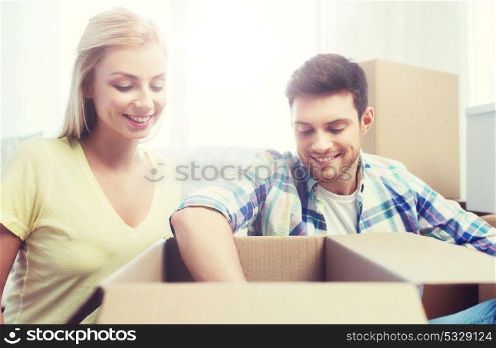 moving, people, repair and real estate concept - smiling couple looking into big cardboard box at new home. smiling couple with big boxes moving to new home