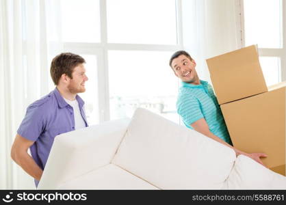 moving, real estate and friendship concept - smiling male friends with sofa and boxes at new home