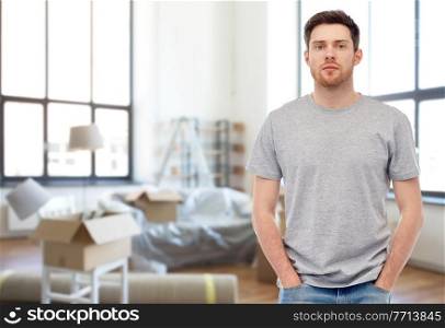 moving, real estate and people concept - young man in gray t-shirt and jeans over new home background. young man in gray t-shirt at new home