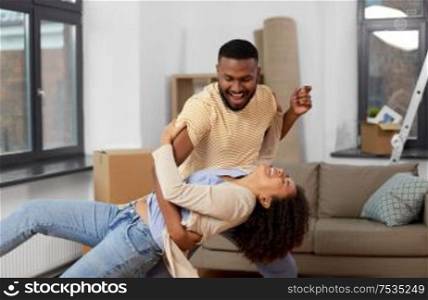 moving, repair and real estate concept - happy african american couple dancing at new home. happy couple moving to new home and dancing