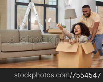 moving, repair and real estate concept - happy african american couple having fun and playing with cardboard box at new home. happy couple moving to new home and having fun