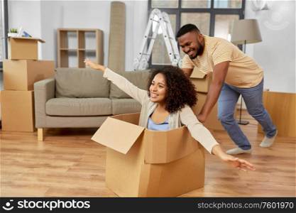 moving, repair and real estate concept - happy african american couple having fun and playing with cardboard box at new home. happy couple moving to new home and having fun