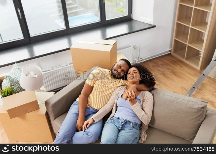 moving, repair and real estate concept - happy african american couple with cardboard boxes sitting on sofa at new home. happy couple with boxes moving to new home