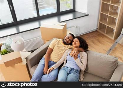 moving, repair and real estate concept - happy african american couple with cardboard boxes sitting on sofa at new home. happy couple with boxes moving to new home