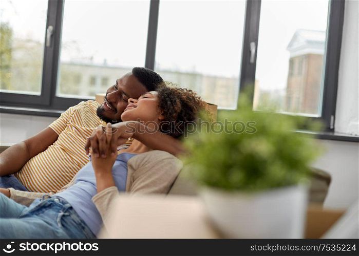moving, repair and real estate concept - happy african american couple with stuff in cardboard boxes hugging at new home. happy couple moving to new home and hugging