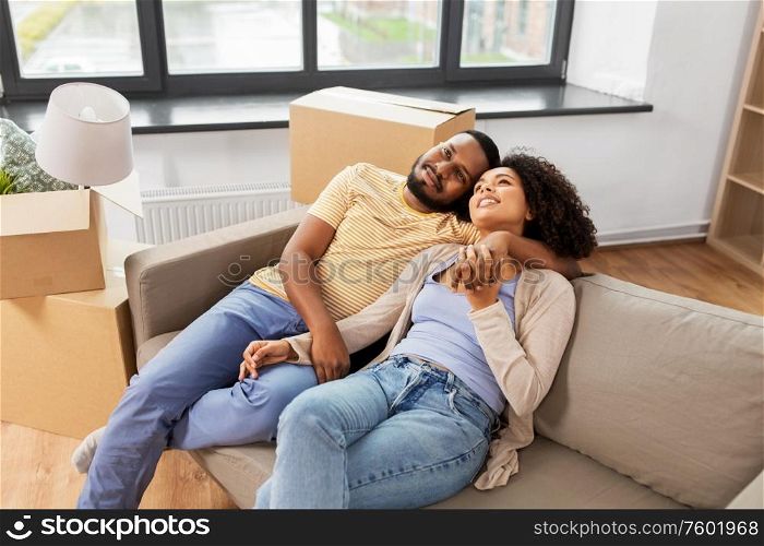 moving, repair and real estate concept - happy african american couple with cardboard boxes sitting on sofa at new home. happy couple with boxes moving to new home