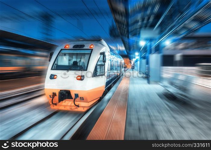 Moving train on the railway station at night. Urban landscape with modern high speed train in motion on the railway platform with illumination at dusk. Intercity vehicle. Passenger railroad travel