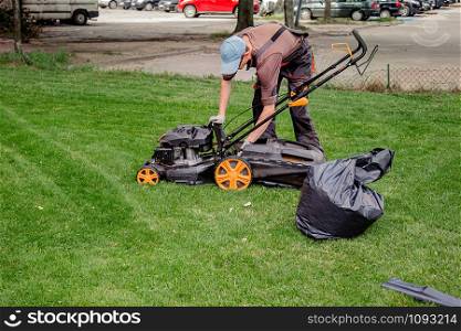 Mowing a household garden lawn with black bag of grass clippings. Worker collects mowed grass in black plastic bags on a recently trimmed lawn. Mowing a household garden lawn with black bag of grass clippings.