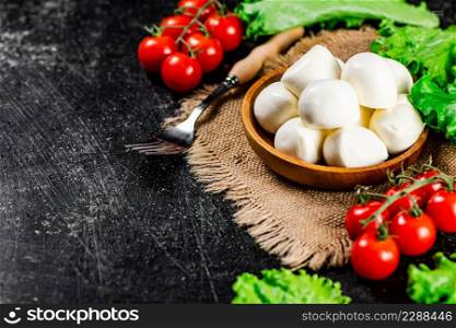 Mozzareella in a plate on a napkin with tomatoes and lettuce. On a black background. High quality photo. Mozzareella in a plate on a napkin with tomatoes and lettuce.