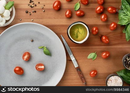 Mozzarella and cherry tomatoes with basil leaves, salt and pepper, layout on a wooden board. The process of preparing Italian Caprese salad. Top view