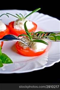 Mozzarella and tomato with rosemary on white plate in black background.