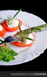 Mozzarella and tomato with rosemary on white plate in black background.