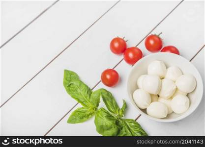 mozzarella cheese ball with basil leaf red tomatoes wooden white background