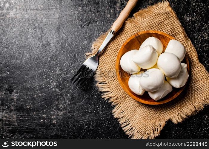 Mozzarella cheese in a wooden plate on a napkin with a fork. On a black background. High quality photo. Mozzarella cheese in a wooden plate on a napkin with a fork.