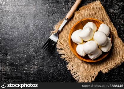 Mozzarella cheese in a wooden plate on a napkin with a fork. On a black background. High quality photo. Mozzarella cheese in a wooden plate on a napkin with a fork.