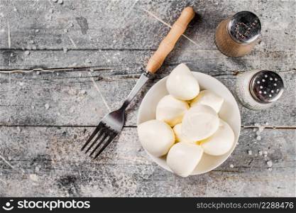 Mozzarella cheese in bowl on a table with a fork. On a gray background. High quality photo. Mozzarella cheese in bowl on a table with a fork.