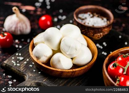 Mozzarella cheese on a cutting board with spices and tomatoes. Against a dark background. High quality photo. Mozzarella cheese on a cutting board with spices and tomatoes.