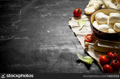 Mozzarella cheese, tomatoes, olive oil and herbs on an old fabric. On a black wooden background.. Mozzarella cheese, tomatoes,
