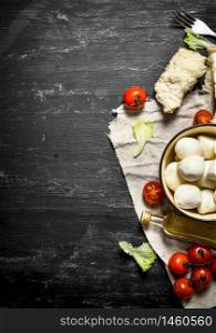 Mozzarella cheese, tomatoes, olive oil and herbs on an old fabric. On a black wooden background.. Mozzarella cheese, tomatoes,