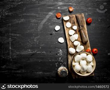 Mozzarella cheese with an old knife and tomatoes. On a black wooden background.. Mozzarella cheese with an old knife and tomatoes.